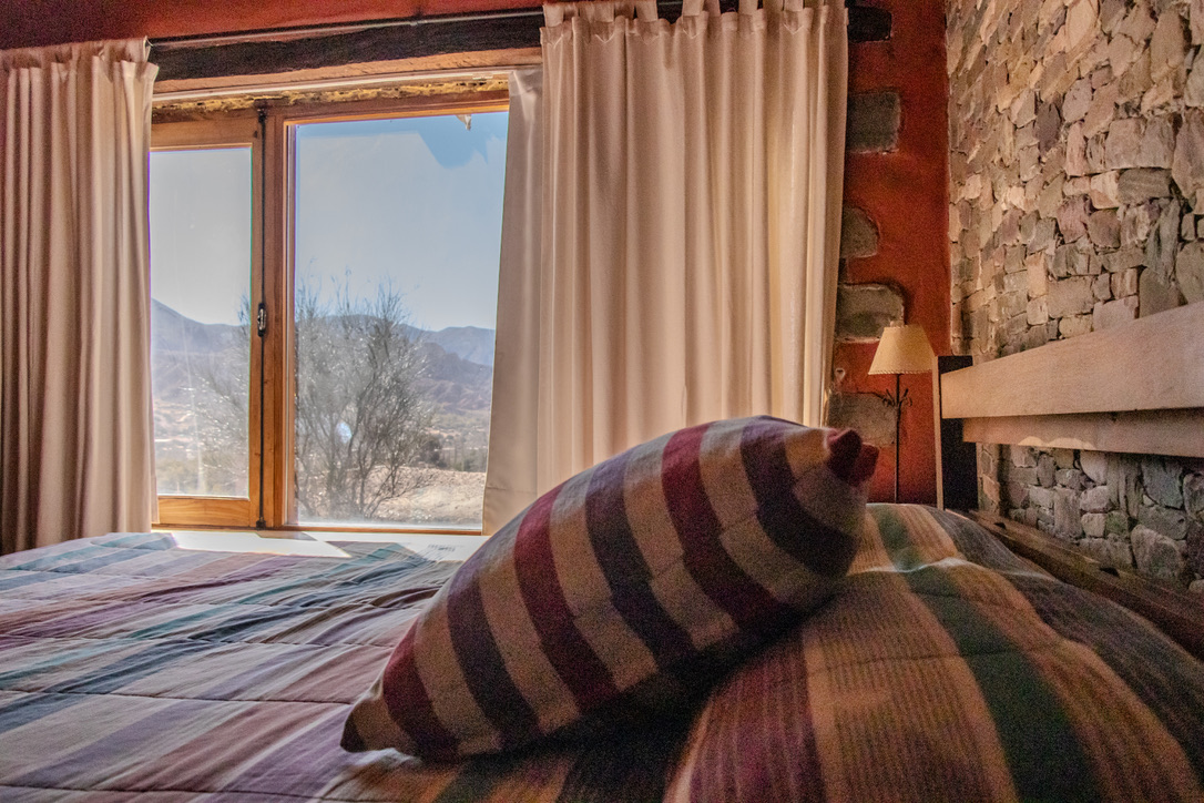 Cama con almohadón andino y vista a los cerros de Tilcara